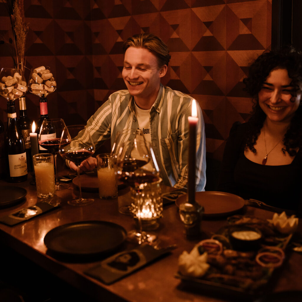 Twee gasten lachen aan een tafel met kaarslicht en borrelhapjes