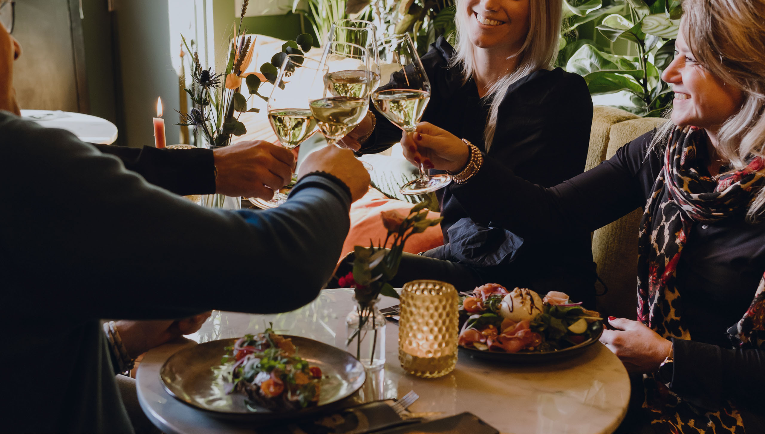 Gezelschap proost met witte wijn boven gerechten die op tafel gedeeld worden